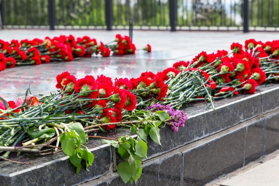 Claveles rojos depositados en un monumento, probablemente en memoria. Flores dispuestas sobre una superficie de piedra oscura.