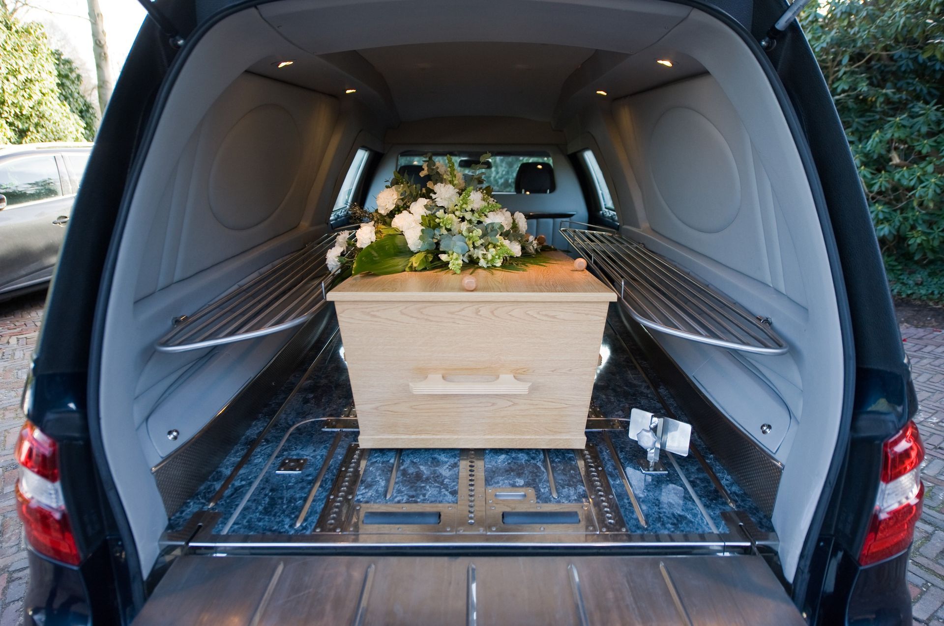 Interior de coche fúnebre con ataúd de madera y arreglo floral.