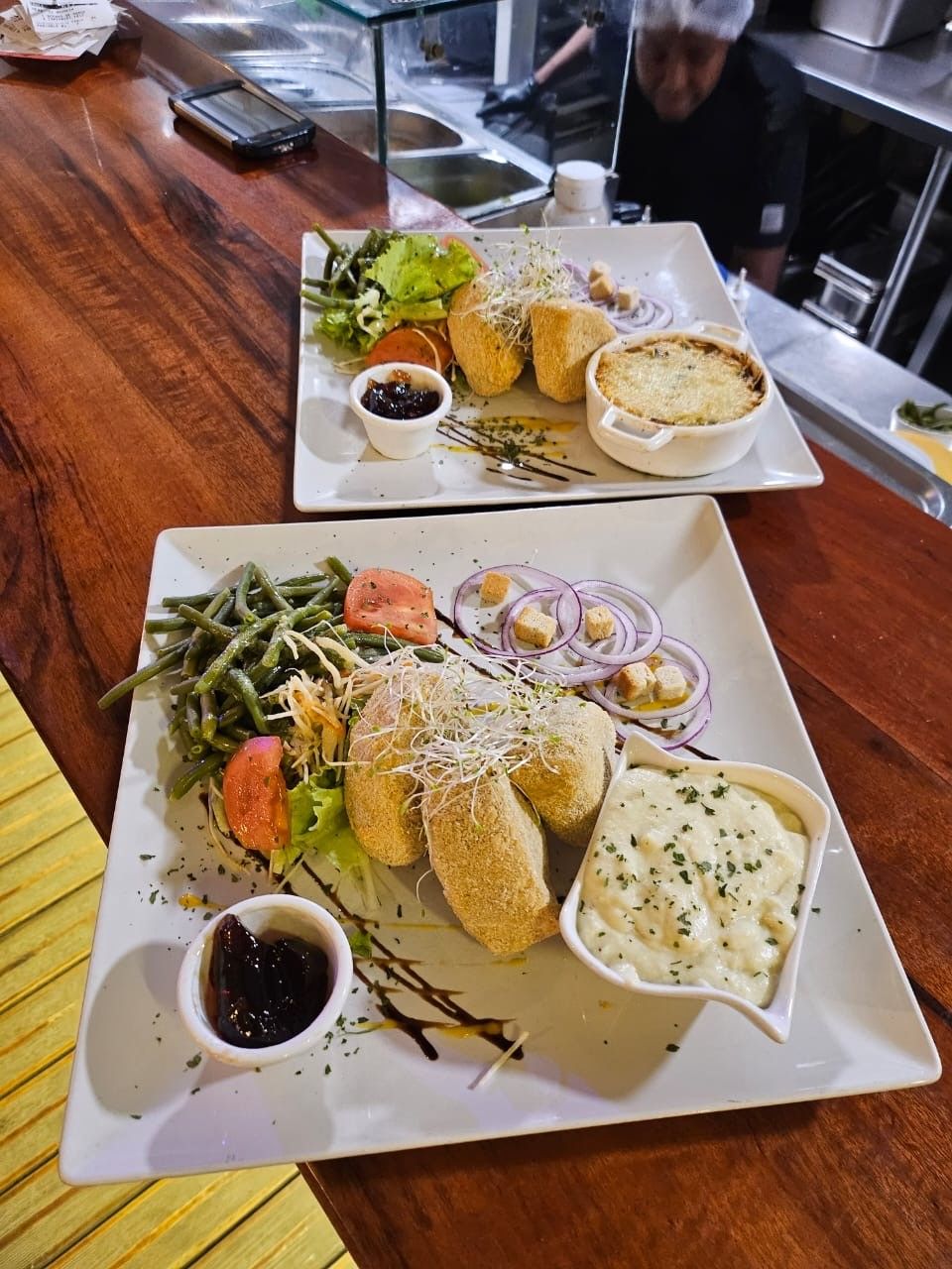 Deux assiettes de nourriture gastronomique : fromage frit, accompagnements de légumes, sauce et un petit plat.