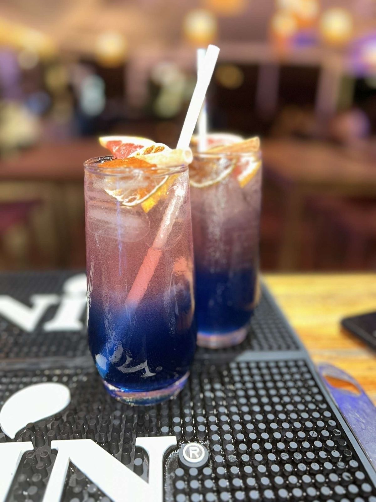 Deux cocktails au dégradé bleu et rose, agrémentés d'agrumes, sur un bar.
