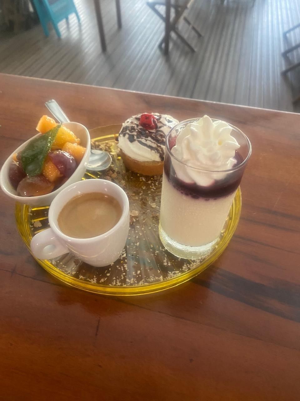 Plateau petit déjeuner : café, salade de fruits, un beignet au chocolat et un parfait dessert sur une assiette dorée.