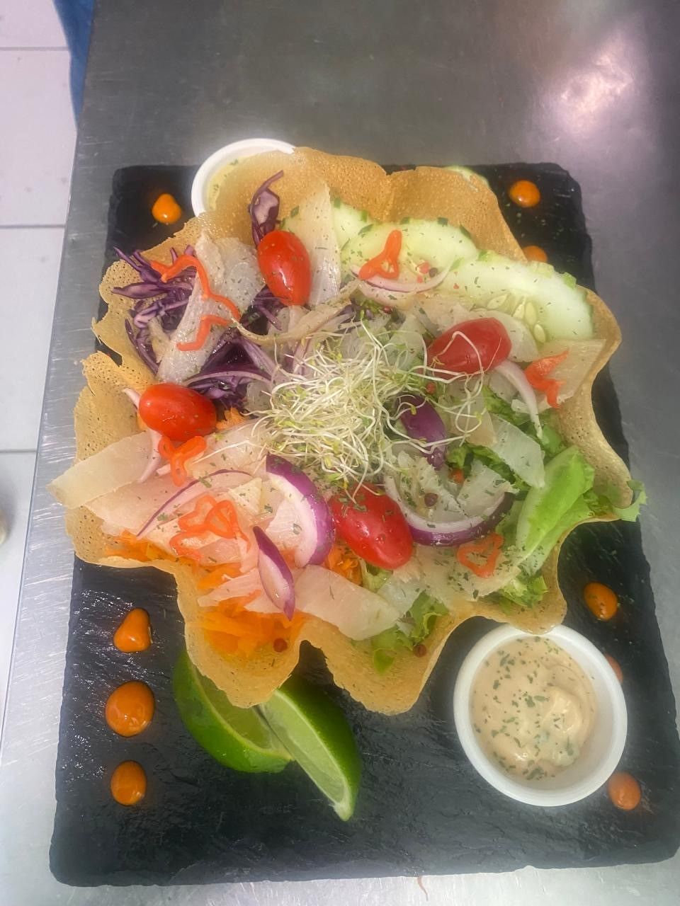 Salade dans un bol de tortilla avec légumes et vinaigrette, servie sur une assiette en pierre noire, avec du citron vert.