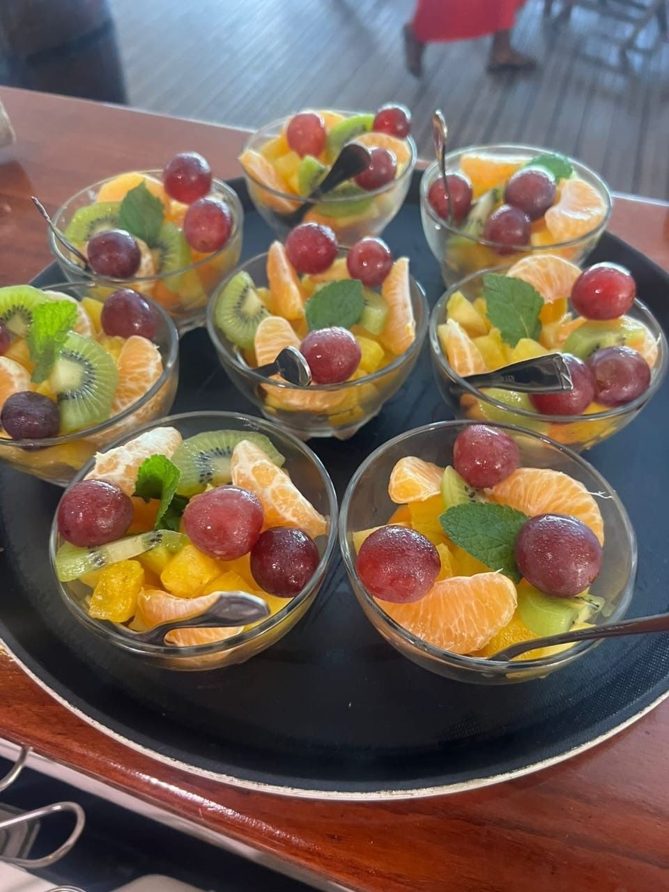 Salade de fruits dans de petits bols en verre sur un plateau, comprenant des raisins, des kiwis et des oranges.