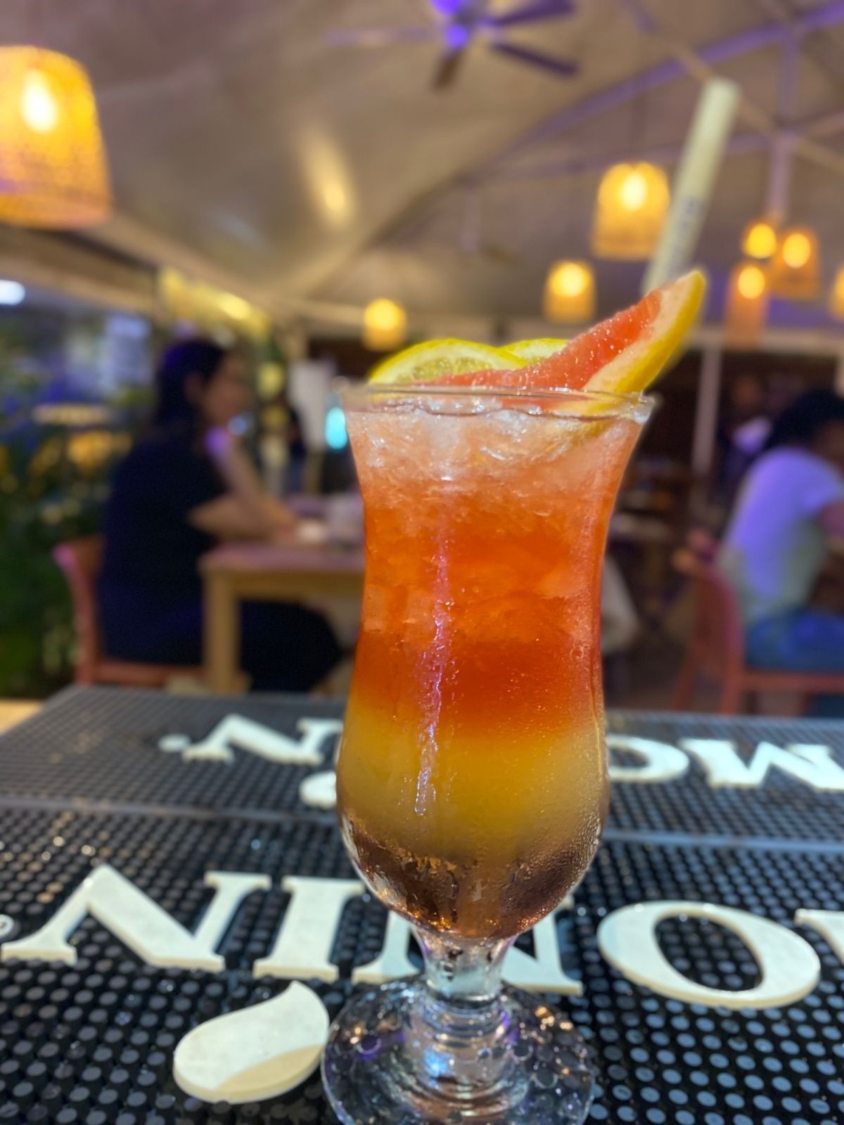Cocktail dans un grand verre, couleurs superposées avec garniture de pamplemousse et de citron, sur un bar.