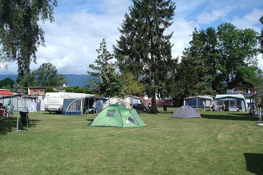 Une tente de camping verte et une petite tente grise sont installées sur un terrain herbeux.