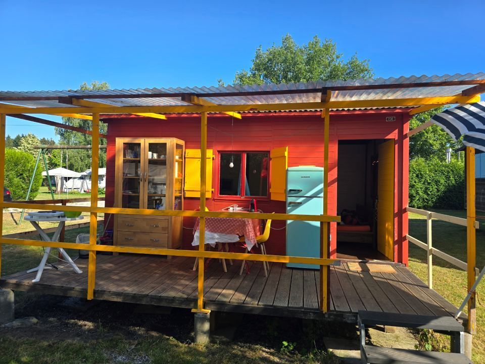 Un chalet rouge vif avec des volets et des garnitures jaunes, doté d'une terrasse en bois.