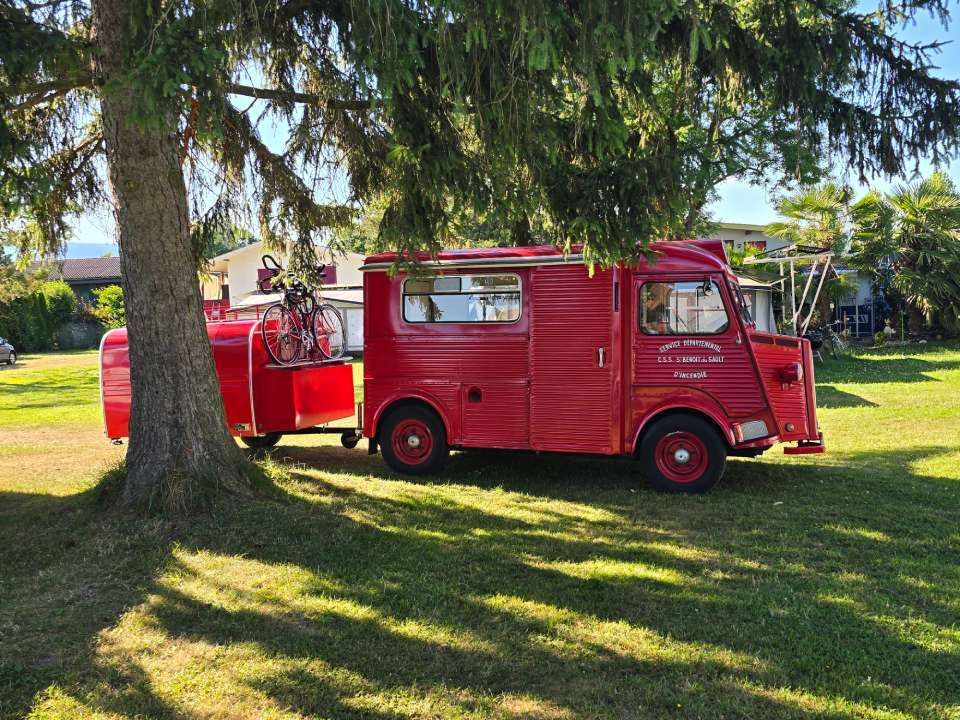 Une fourgonnette Citroën HY rouge vintage, tractant une remorque rouge assortie.