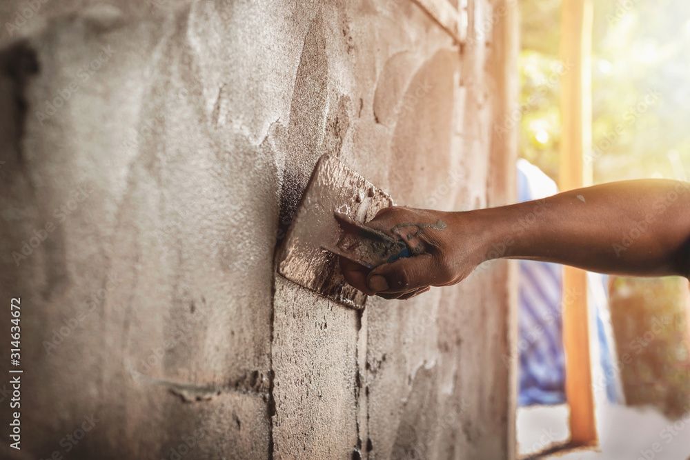 Un uomo sta intonacando un muro con una cazzuola.