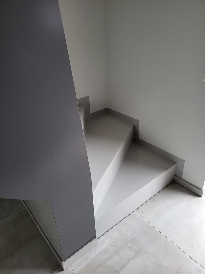 Scala in cemento grigio che porta a un angolo, con una parete grigia e pareti bianche.