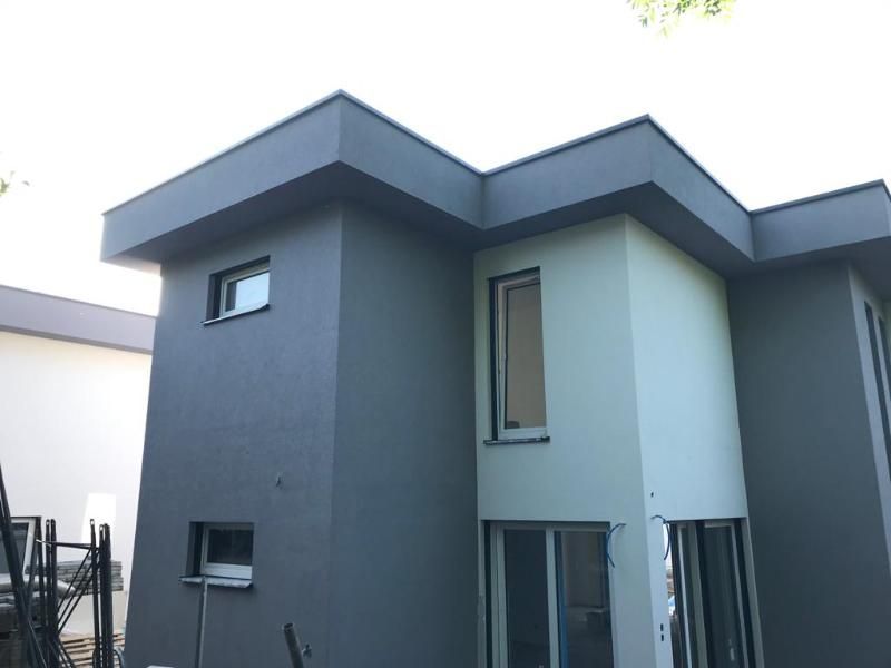 Moderna casa a due piani con pareti esterne grigio scuro e grigio chiaro, finestre e tetto piano.