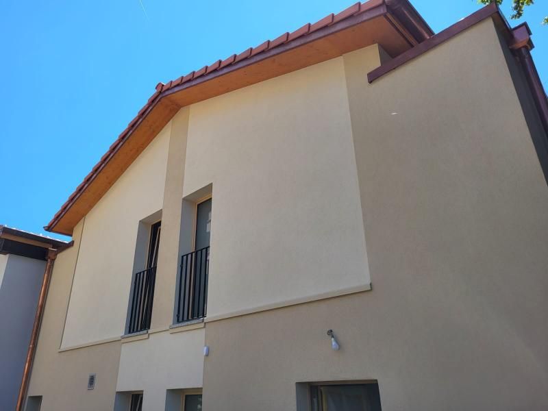 Edificio color marrone chiaro e beige con tetto di tegole rosse e due balconi contro il cielo azzurro.