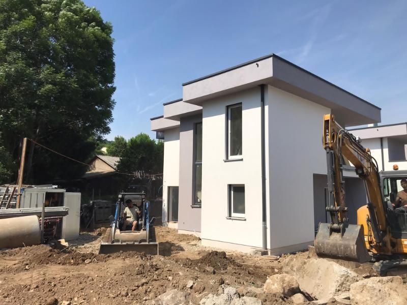 Cantiere con case moderne a due piani. Escavatore e minipala lavorano sullo sterrato. Cielo sereno.