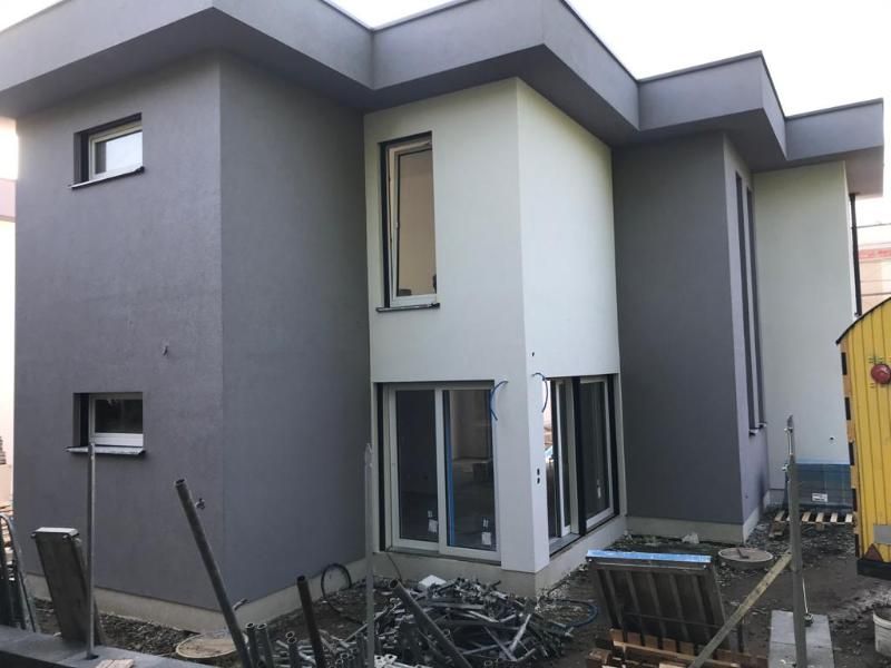 Moderna casa a due piani in costruzione, con pareti esterne grigie e bianche e ampie finestre.