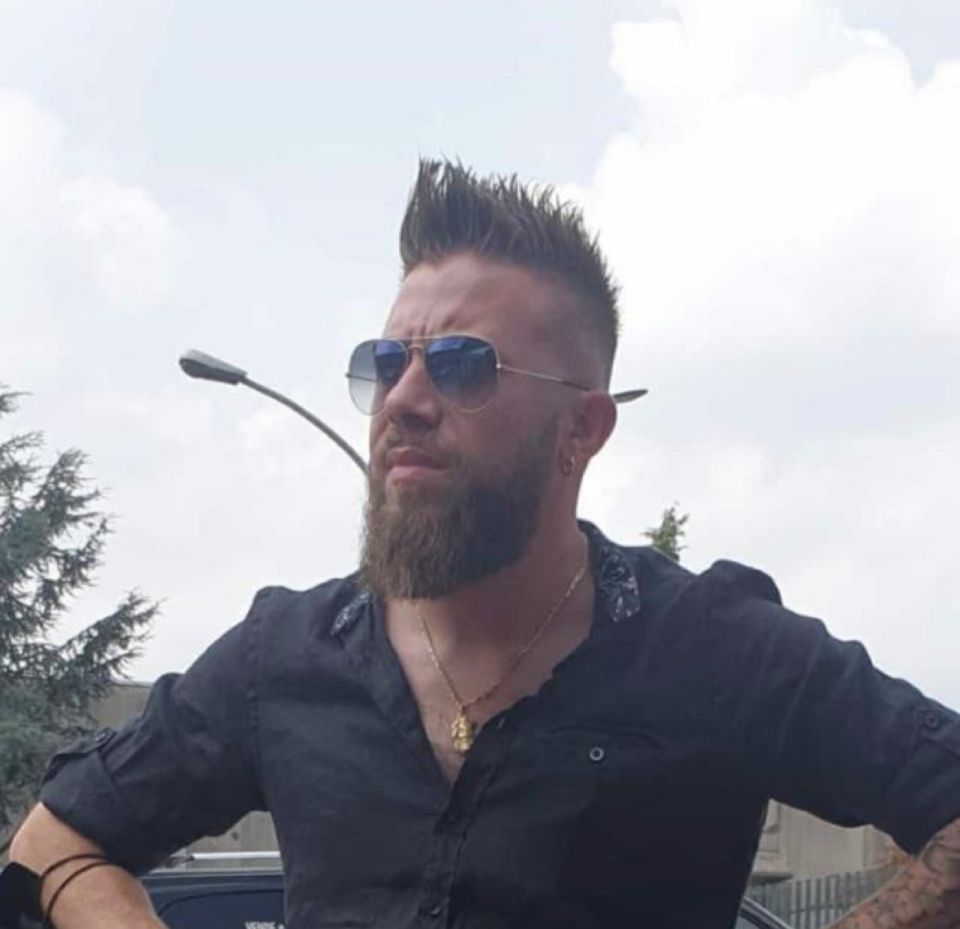 Un uomo con la barba che indossa occhiali da sole e una camicia nera.