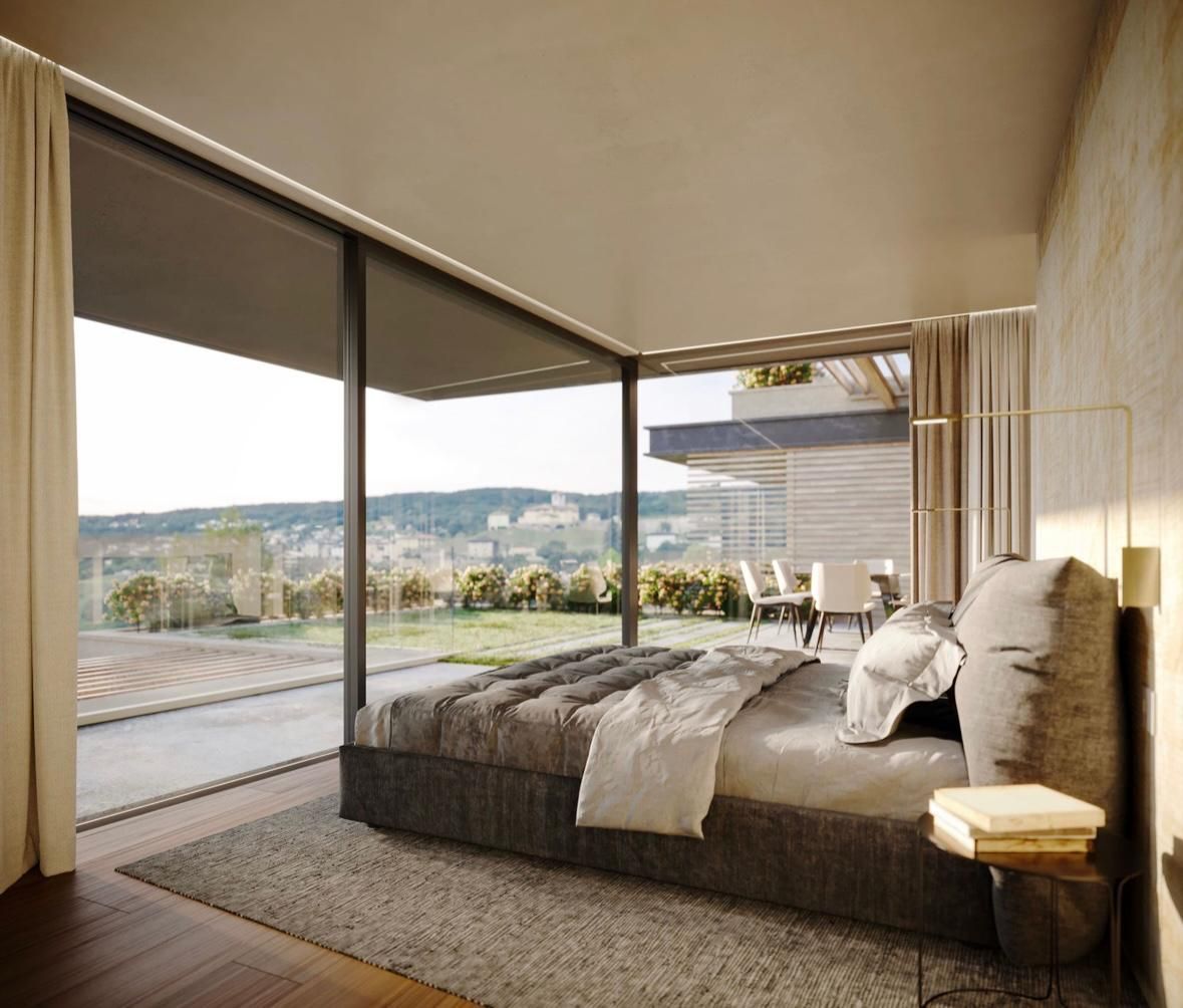 Camera da letto con ampie finestre che si affacciano sul paesaggio; sono visibili un letto con lenzuola grigie e un tavolino.