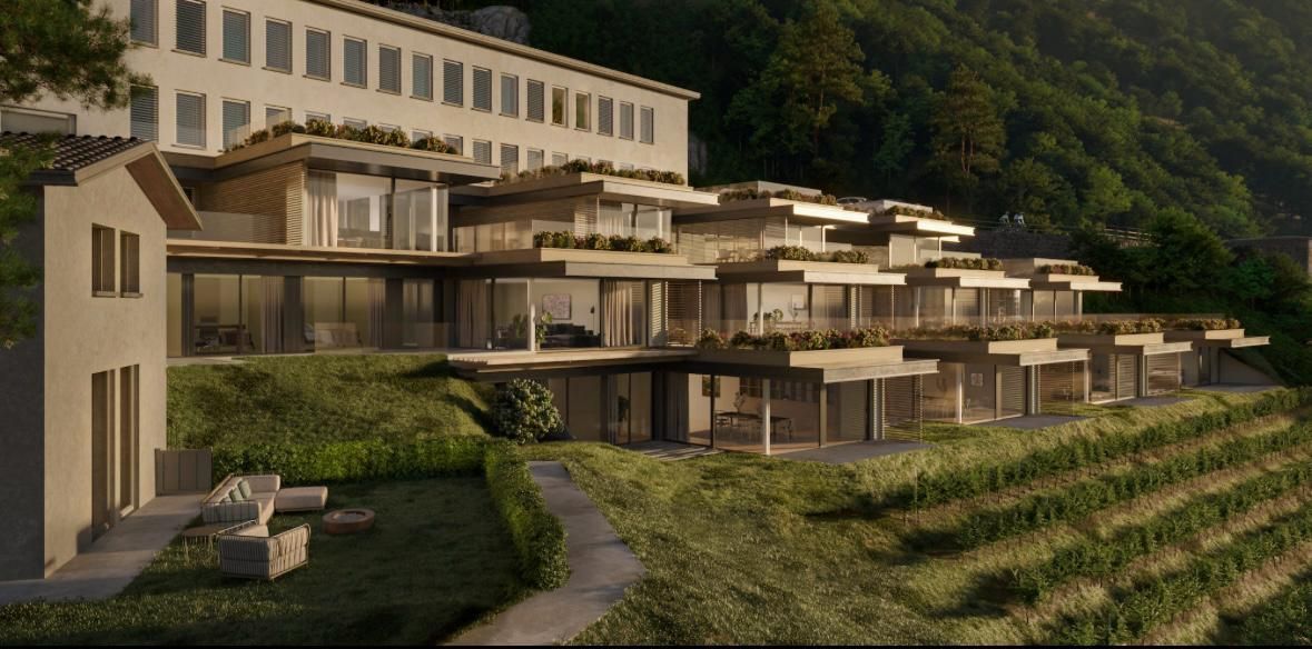 Un moderno hotel in collina con più livelli, un rigoglioso vigneto e le montagne sullo sfondo.