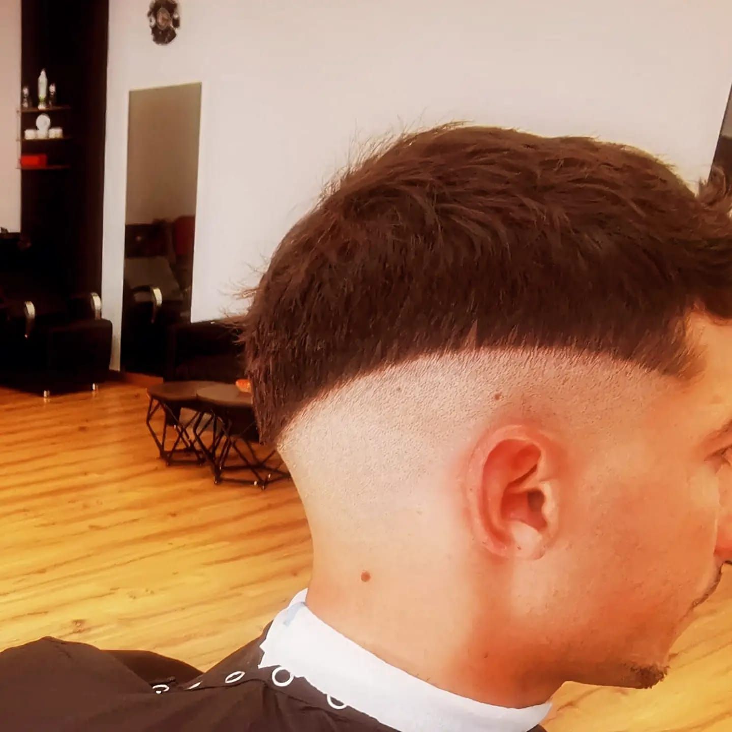 Vista lateral de un corte de pelo corto degradado en una barbería, que muestra la parte superior oscura y los lados afeitados.