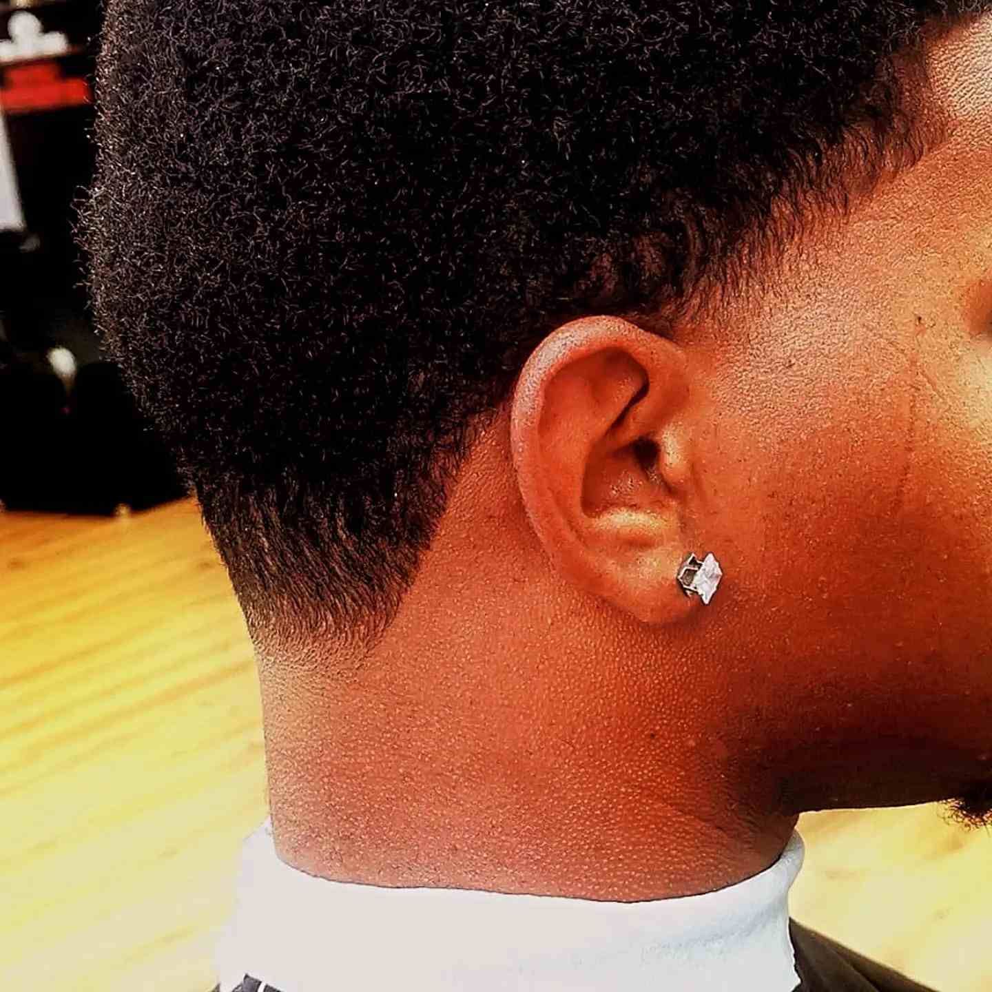 Primer plano de la oreja y el cuello de una persona con un pendiente de diamante, sobre un fondo interior cálido.