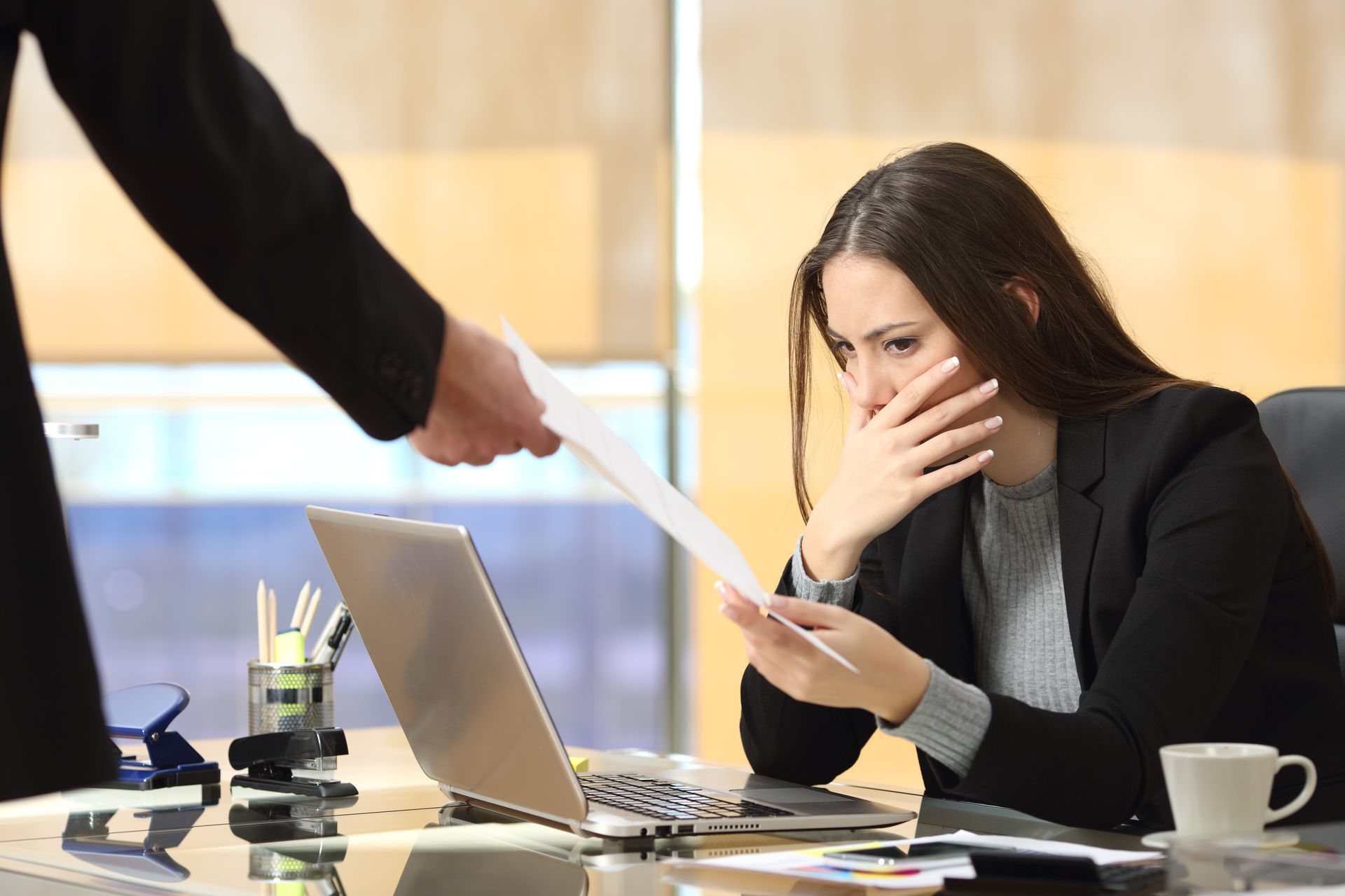Une personne tend un document à une femme assise à un bureau qui présente un air inquiet.