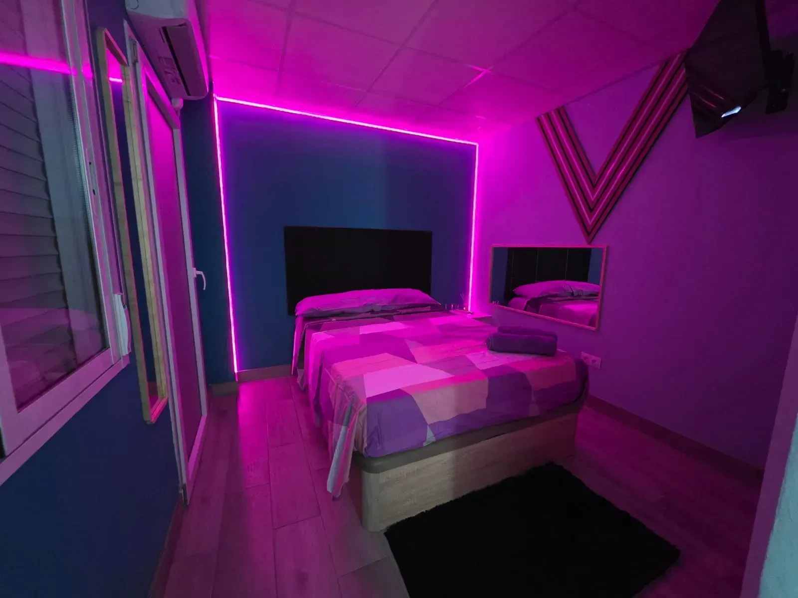 Un dormitorio con una cama y luces violetas en las paredes.