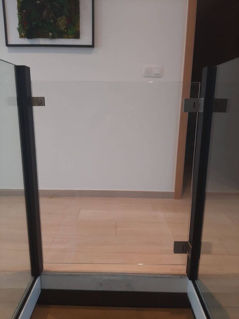 Une barrière d'escalier en verre avec des poteaux en métal noir, fixée sur un parquet clair à l'intérieur d'une maison.