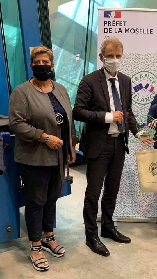 Un homme et une femme en costume et masques se tiennent à côté d'une bannière du préfet de la Moselle.
