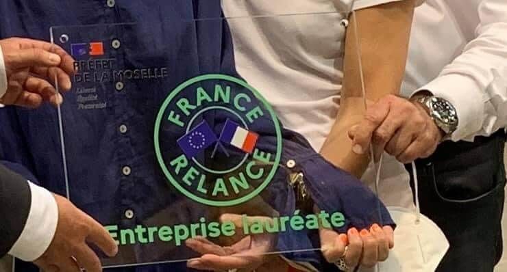 Trois personnes tenant une plaque transparente portant le logo de France Relance et le texte « Entreprise lauréate ».