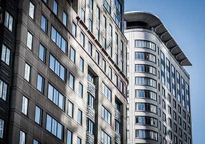 Deux immeubles de grande hauteur mitoyens se détachant sur un ciel bleu clair, avec des façades en pierre et des rangées de fenêtres rectangulaires.