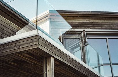 L'extérieur d'une maison moderne se caractérise par un bardage horizontal en bois foncé, une balustrade de balcon en verre et de grandes fenêtres.