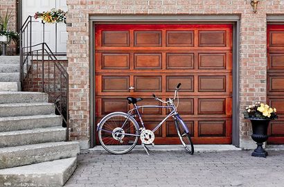 Un vélo est garé devant une porte de garage en bois, à côté de marches en béton et d'une urne à fleurs.
