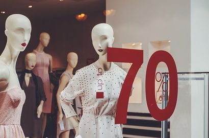 Dans la vitrine d'un magasin, des mannequins arborent une grande affiche rouge jusqu'à 70 % de réduction apposée sur le verre.