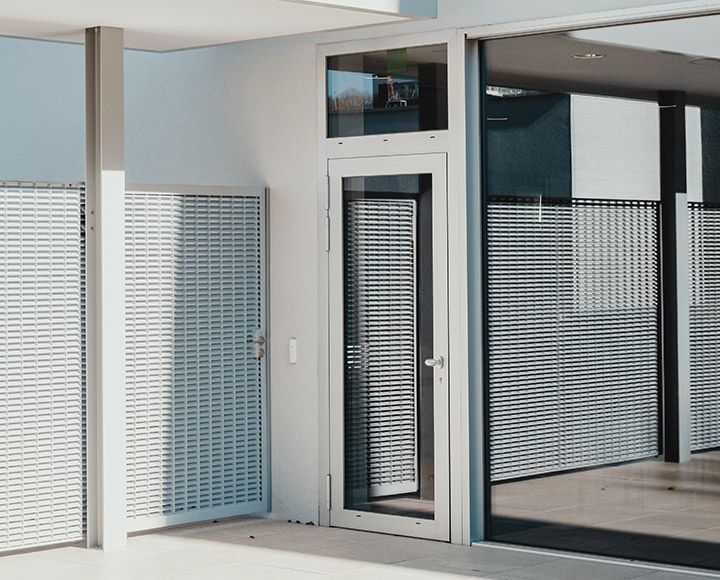 L'extérieur d'un bâtiment moderne, de couleur blanche, est doté d'une porte vitrée et de panneaux d'intimité métalliques à lattes allant du sol au plafond.