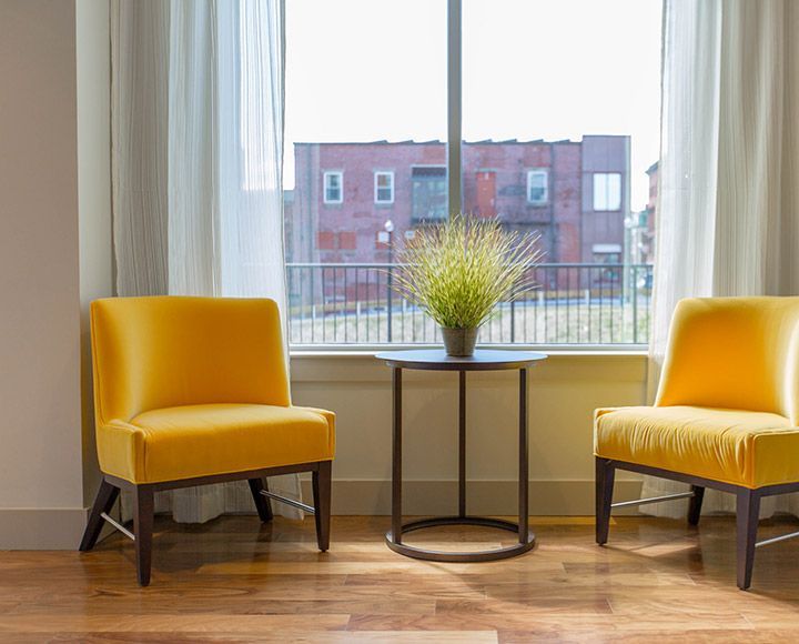 Deux fauteuils jaunes se font face, une petite table et une plante en pot étant placées entre eux, devant une grande fenêtre.