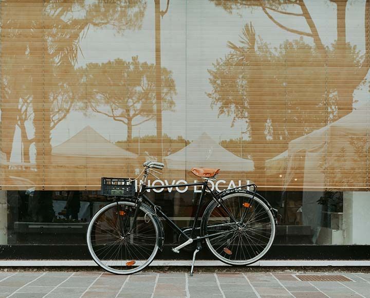Un vélo noir de style vintage, équipé d'un panier avant, est garé sur une rue pavée, devant la vitrine d'un magasin.