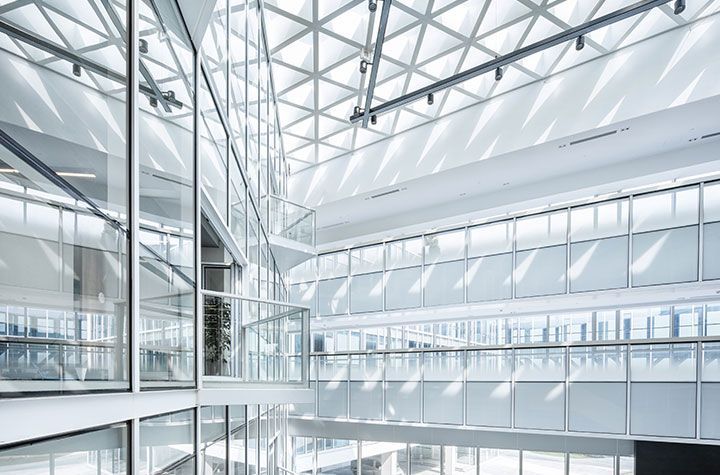 Atrium de bureaux moderne avec un plafond en verre et des balcons étagés, caractérisé par une architecture minimaliste, blanche et lumineuse.