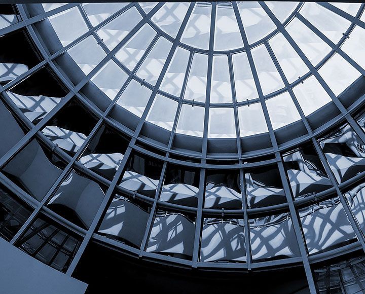 Un plafond circulaire en forme de dôme de verre avec une structure en grille métallique, éclairé par une lumière et des reflets aux tons bleutés.