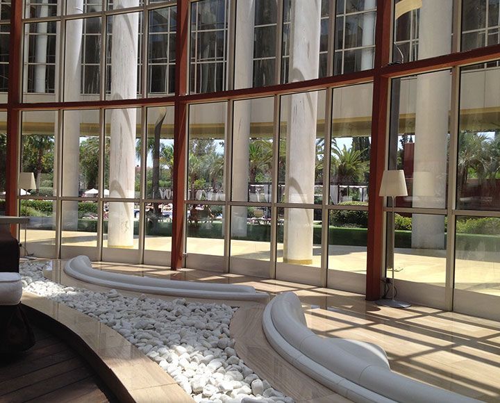 Un coin salon blanc incurvé, au sol recouvert de pierres, donne sur un jardin luxuriant et ensoleillé grâce à des baies vitrées.