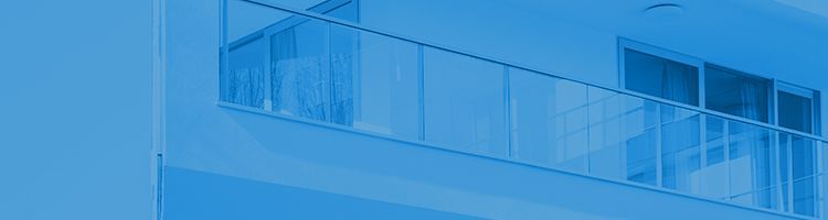 Balcon d'un immeuble moderne avec une rambarde en verre et des fenêtres teintées bleutées.