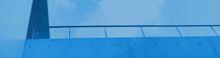 Une rambarde métallique surplombe un mur de béton lisse aux reflets bleutés, se détachant sur un ciel bleu clair.