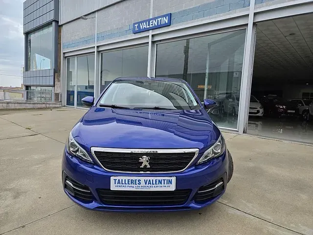 Un Peugeot 308 azul está aparcado delante de un concesionario de automóviles.