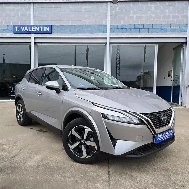 Un Nissan Qashqai plateado está estacionado frente a un concesionario de automóviles.