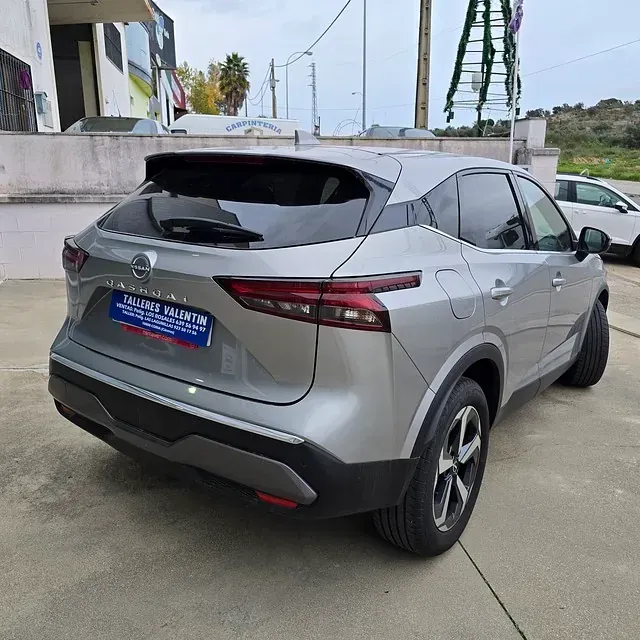 Un Nissan Qashqai plateado está estacionado frente a un edificio.