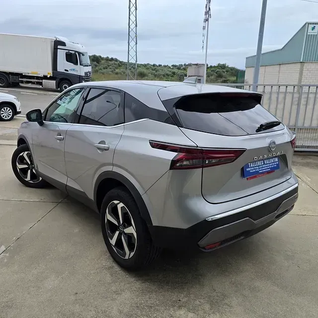 Un coche plateado está aparcado en un estacionamiento con un camión al fondo.