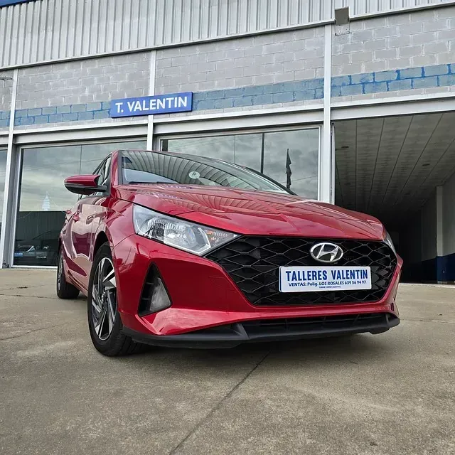 Un coche rojo está aparcado delante de Talleres Valentín.