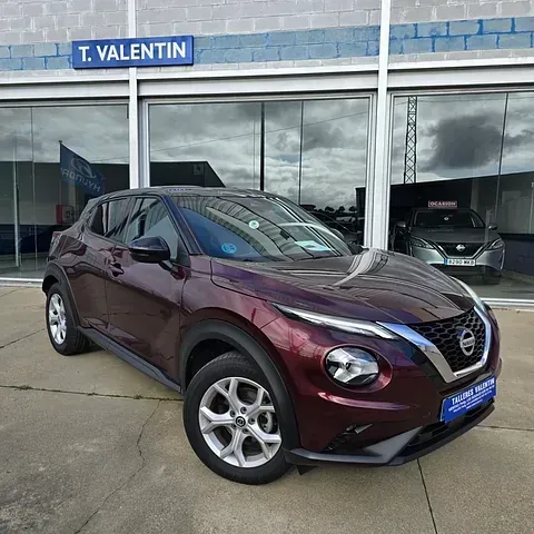 Un Nissan Juke rojo está estacionado frente a un concesionario de automóviles.