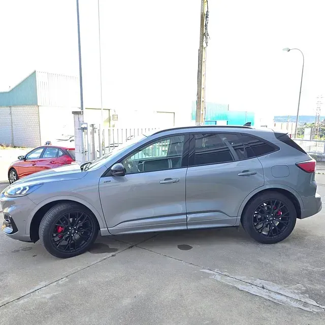 Un coche gris está aparcado en un estacionamiento al lado de un coche rojo.