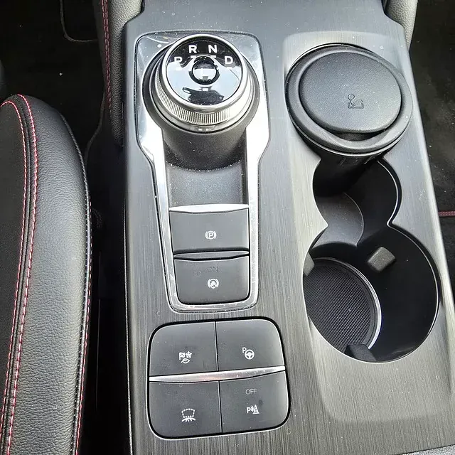 La consola central de un automóvil tiene una palanca de cambios y un portavasos.