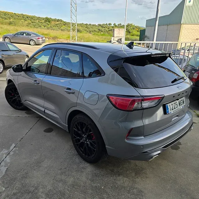 Un coche gris está estacionado al costado de la carretera frente a un edificio.