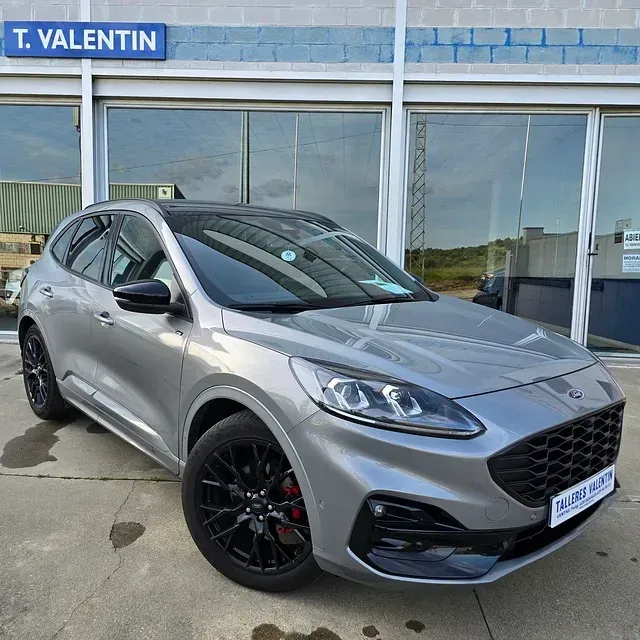 Un Ford Escape plateado está estacionado frente a un concesionario de automóviles.