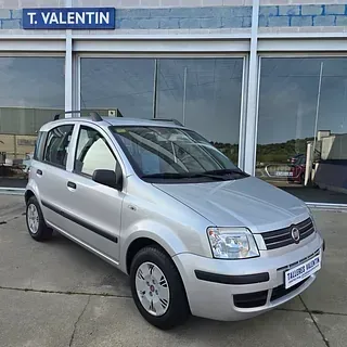 Un coche plateado está aparcado delante de un concesionario de automóviles.